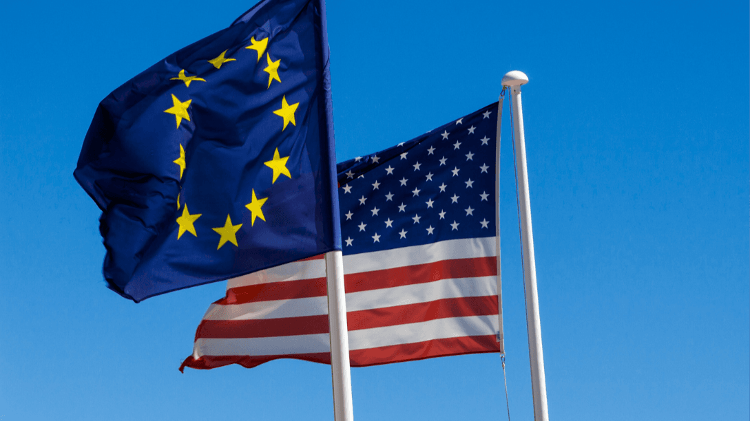 European Union and United States flags against a clear blue sky.