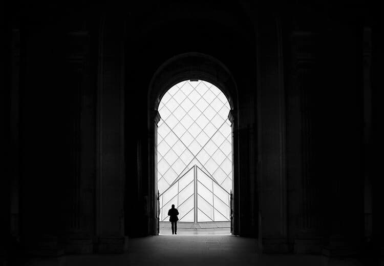 A silhouetted figure standing beneath a vast arched passageway and luminous geometric window.